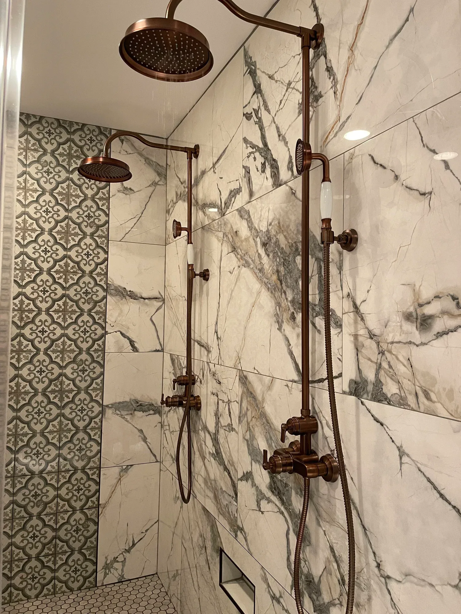 Luxury walk-in shower with marble slab walls, patterned accent tile, and antique copper fixtures, remodeled by Hale Development